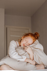 Red-haired girl sleepily hugs a pillow