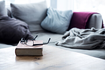 book with eyeglasses on wooden table in front of cozy couch