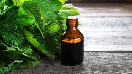 Nettle extract in a medical bottle and fresh nettle leaves on a vintage wooden background, medical concept about the benefits of medicinal herbs