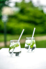 Beautiful glass of water or mojito with lime and mint cocktail on the gree background and white table summer vibe and atmosphere