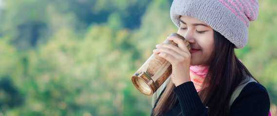 A beautiful young Asian traveler is drinking coffee from a bamboo tube.