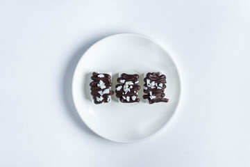 White marshmallow poured by dark chocolate. Three marshmallows on a white plate. Dessert of the aristocrat. Photo from above.