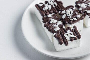 Several white marshmallows poured with dark chocolate. marshmallows on a white plate. Dessert of the aristocrat.