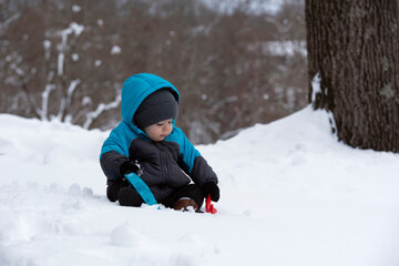 Fototapeta na wymiar 1 year old baby boy bundled up and playing in the snow with toys