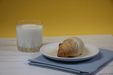 croissant on a plate on a blue napkin and a glass of milk on wooden table