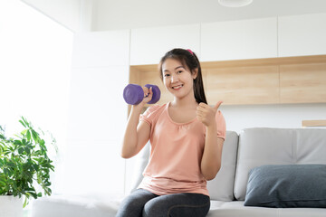 Fototapeta na wymiar Asian women happy exercise with dumbbell workout at home in free time show hand thumb up 
