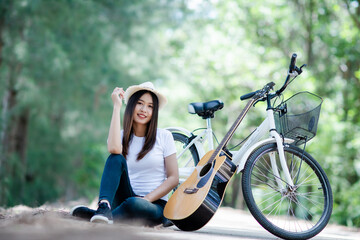 Naklejka na ściany i meble Portrait of beautiful girl playing the guitar with bike at nature background