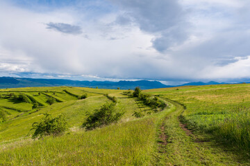 Fototapeta na wymiar Gathering storm clouds over green hills , dirt road in the Carpathian mountains, Romania.