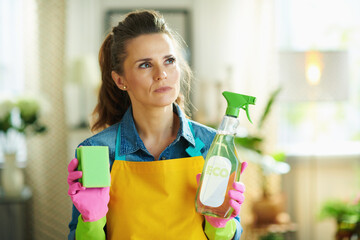 pensive woman with cleaning agent and sponge