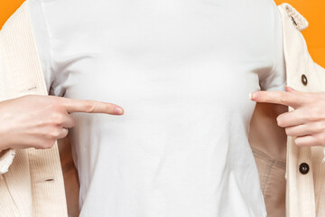 Female hands point to a white t-shirt isolated over an orange background, mockup, empty space for text, logo, design, print, close up