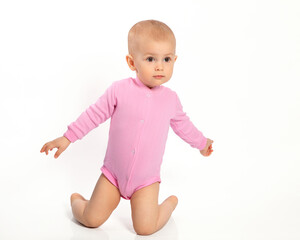 A little European girl baby is on her knees and spread her arms on a white background. Portrait of a cute little girl, a happy child.