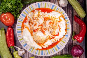Delicious Eggs with yogurt, red pepper and butter sauce, cilbir, served on a white plate on a white plate. Top view