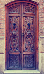 An ornately carved and decorated dark wooden door with two busts in military helmets and two metal door knockers of a residential property in the old quarter of Granada, Southern Spain
