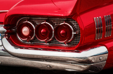 Rear part of exterior of a red old timer luxury sports car with tree tail lights framed in chrome...