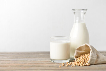 Glass of soy milk with bottle and soybeans on wooden table.