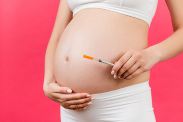 Close up of pregnant woman holding insulin syringe against her belly at colorful background with copy space. Diabetes concept