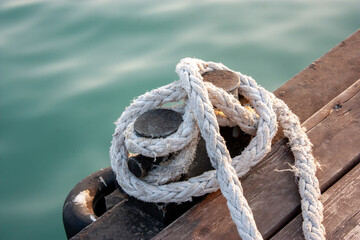 Fototapeta premium A black bollard on a wooden pier is wrapped in a mooring rope. Side view. Knecht is a pair of cast-iron pedestals. Knecht for mooring and securing mooring cables.