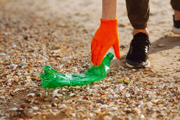 Young male volunteer picks up plastic garbage on the ocean coast. A man collects waste on the seaside to save ecology and protect environment. Recycle litter and pollution concept.