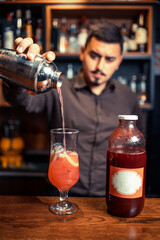 Elegant, young bartender pouring red cocktail from the shaker to the glass