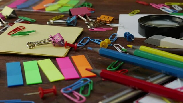 Assortment of school stationery on brown wooden table: multi-colored pencils, paper clips, chips, smiles binder clips. Back to school, education or knowledge concept