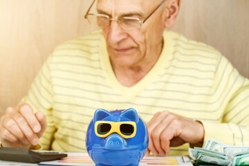 elderly man in glasses counts on calculator at piggy bank