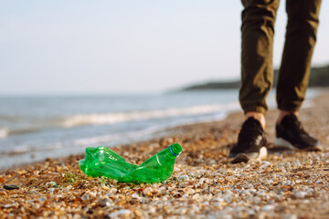 Young male volunteer picks up plastic garbage on the ocean coast. A man collects waste on the seaside to save ecology and protect environment. Recycle litter and pollution concept.