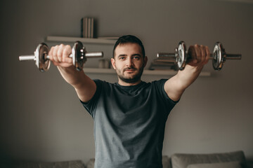Naklejka na ściany i meble beautiful man doing exercises for biceps hands with metal dumbbells. Sport in quarantine at home. 