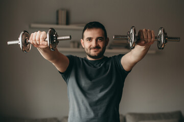 beautiful man doing exercises for biceps hands with metal dumbbells. Sport in quarantine at home. 
