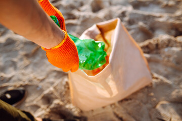 Young male volunteer picks up plastic garbage on the ocean coast. A man collects waste on the seaside to save ecology and protect environment. Recycle litter and pollution concept.