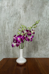 Purple Orchid is in a white vase on a wooden table on grey background
