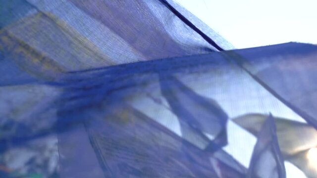 Many large colored prayer flags - the Lungta, with Buddhist mantras in Tibetan, are slowly fluttering in the wind in sun backlight.