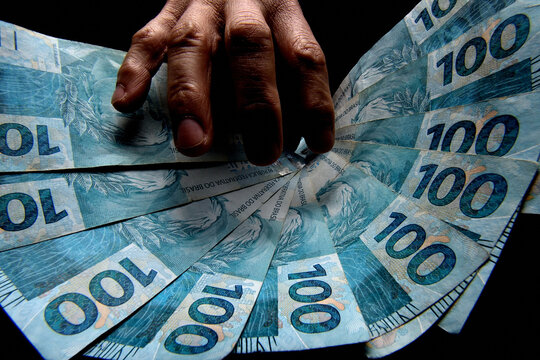 Notas de cem reais brasileiros e m&atilde;o de homem no escurid&atilde;o