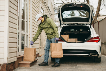 Delivery man in a medical mask and gloves delivers the parcel to house, leaves packages at the...