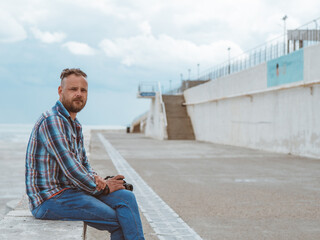 Fototapeta na wymiar bearded hipster man with mohawk sits on a concrete bench near the sea on the waterfront.