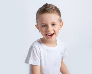 A beautiful European boy in a white t-shirt on a white background. A blue-eyed child of five years old smiles and laughs. Children's emotions.