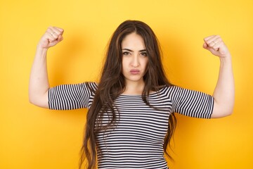 Waist up shot of caucasian woman raises arms to show her muscles feels confident in victory, looks...