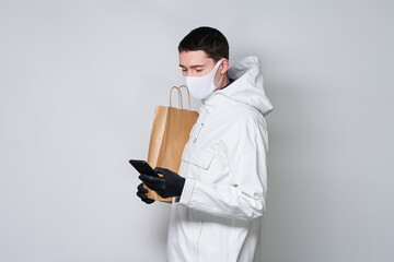 Man wearing a protective mask to prevent the spread of Coronavirus hold shopping bag and communicates via smartphone.