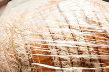 Pre sliced bread with flour in a simple see through transparent plastic bag container, tightly wrapped, macro, closeup. Unecological not eco friendly food packaging. Abstract background texture