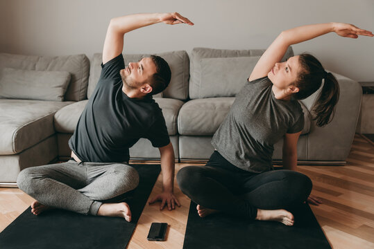 Young happy couple doing yoga on quarantine at home. Stretching, exercise, health