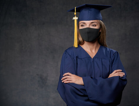 Young Female Graduate Both Hands On The Side Celebrating Her University Degree Wearing Blue Cap And Gown Also Wearing Black Mask