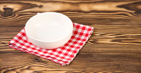 
Empty white plate on checkered cotton napkin on a wooden table