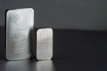 Two different silver bullion on a gray background. Selective focus.