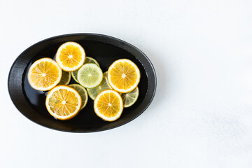 fresh and juicy sliced lemon and lime slices in water, in a black bowl on a white background, citrus background. beauty and health concept.