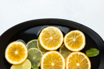 fresh and juicy sliced lemon and lime slices in water, in a black bowl on a white background, citrus background. beauty and health concept.