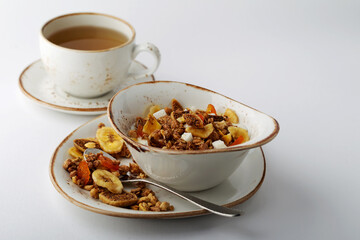 Authentic muesli and a cup of tea sprinkled with cinnamon on a white tablecloth. Morning atmospheric lighting, fashionable trendy spot soft focus. Preparation for design creative menu.