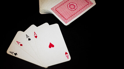 Obraz premium Ángulo levemente elevado de un juego de ases de poker aislados sobre un fondo negro y con iluminación directa sobre ellos. Junto se encuentra un mazo de cartas de fondo rojo. 