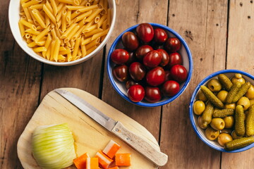 Ingredients for a pasta salad on an old wooden table, tomatoes, olives, pickles, crab sticks, onion and macaroni