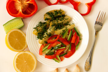 Fried potatoes with bell pepper, cucumber and herbs on a white plate. View from above. White background..l