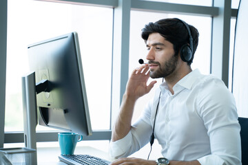 Smiling handsome young male call centre operator with headset.Confident male customer service representative,operator,agent,call centre worker,support staff speaking with head set in modern office