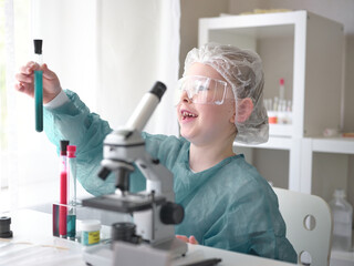 Cute little girl looking into microscope at his desk at home. Young scientist making experiments in...